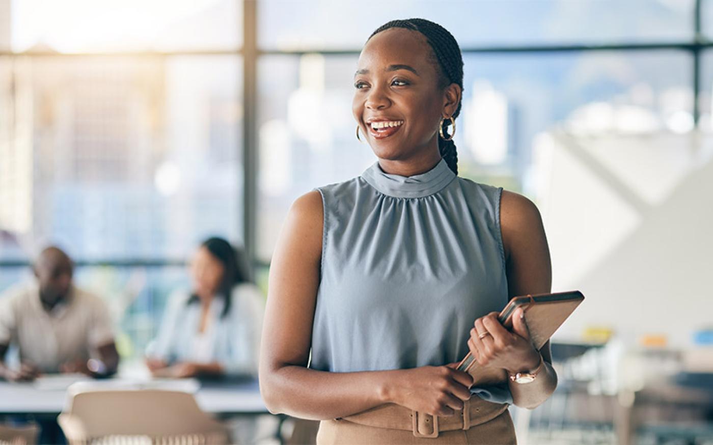 A woman standing and smiling in a busy office building.